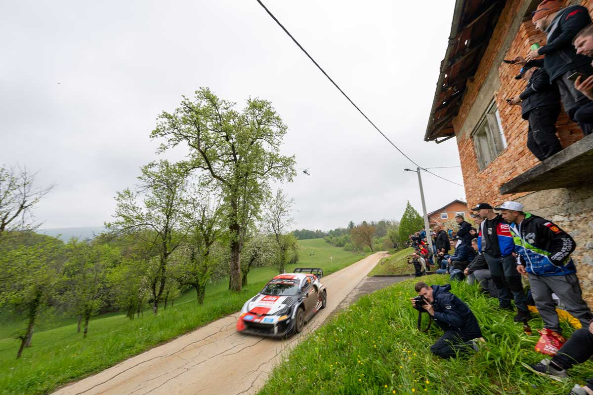 Público y fotógrafos muy cerca del paso de un coche de rally junto a una casa en el tramo